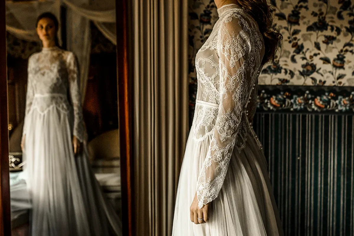 Braut im Spitzenkleid und Schleier in einem dunklen historischen Innenraum