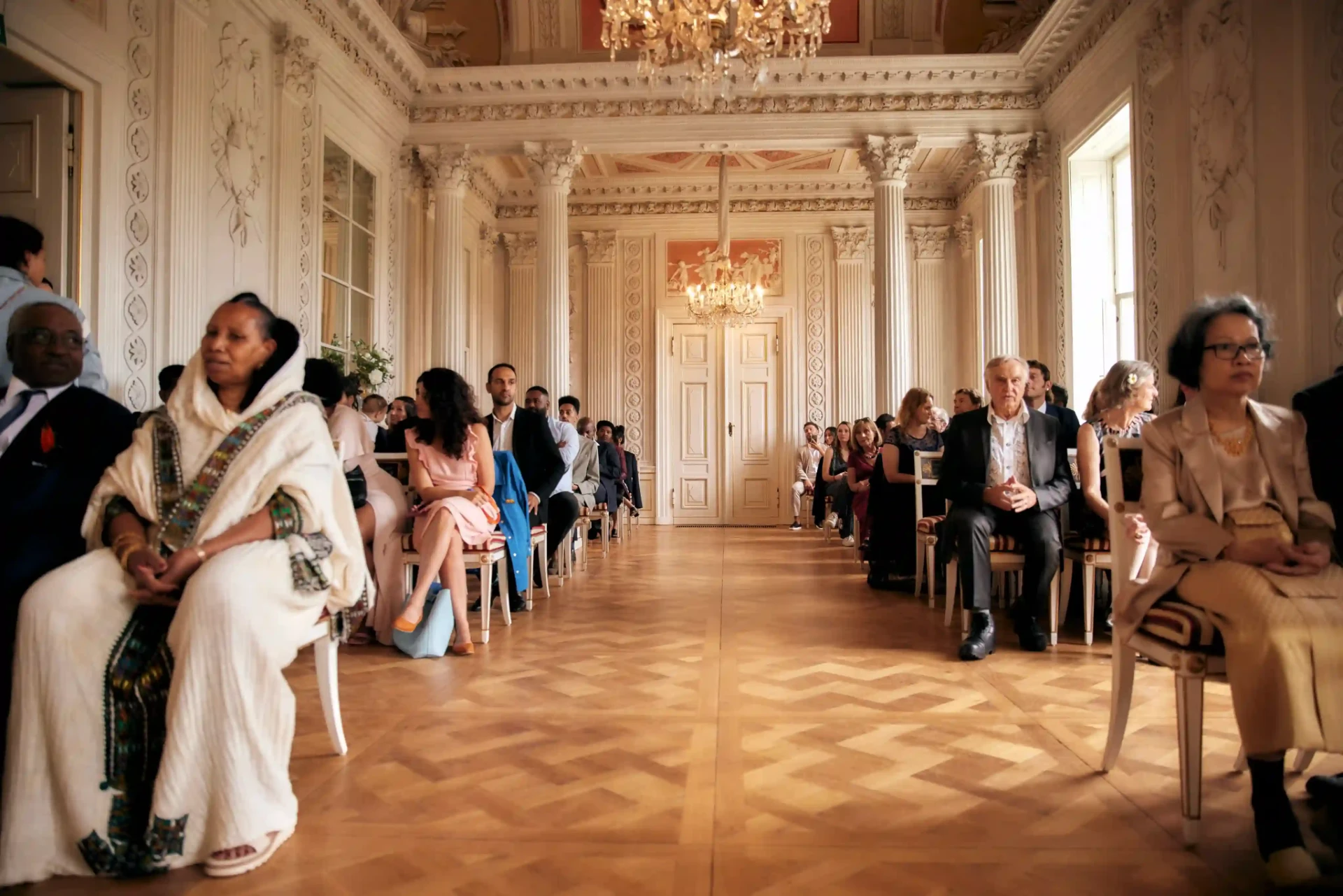 Wedding couple walking past seated guests in an ornate hall