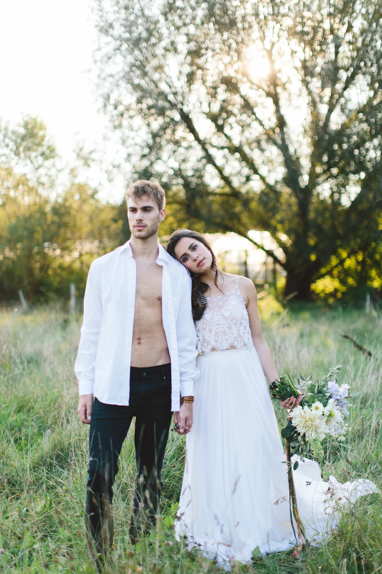 Bride leaning her head against the groom while standing together in a meadow