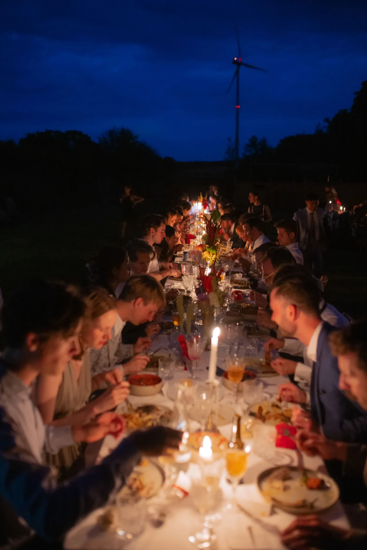 Outdoor wedding dinner at dusk with guests seated at a long table