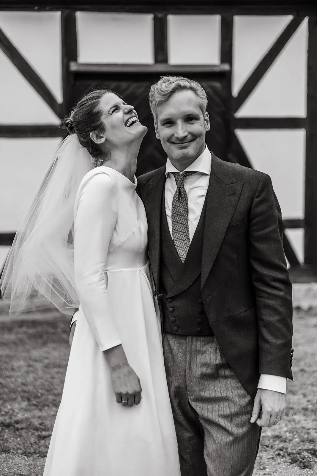 Bride and groom smiling outside a half-timbered house, black-and-white photograph