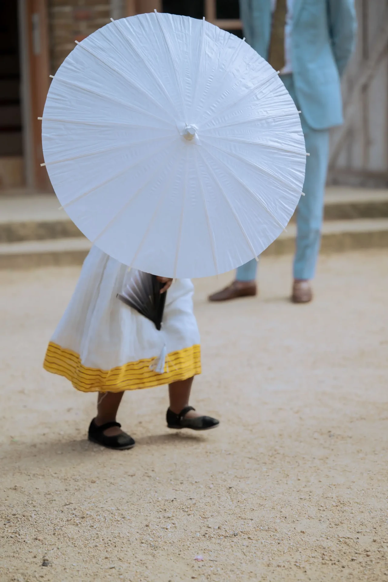 Person carrying a white parasol on a gravel path