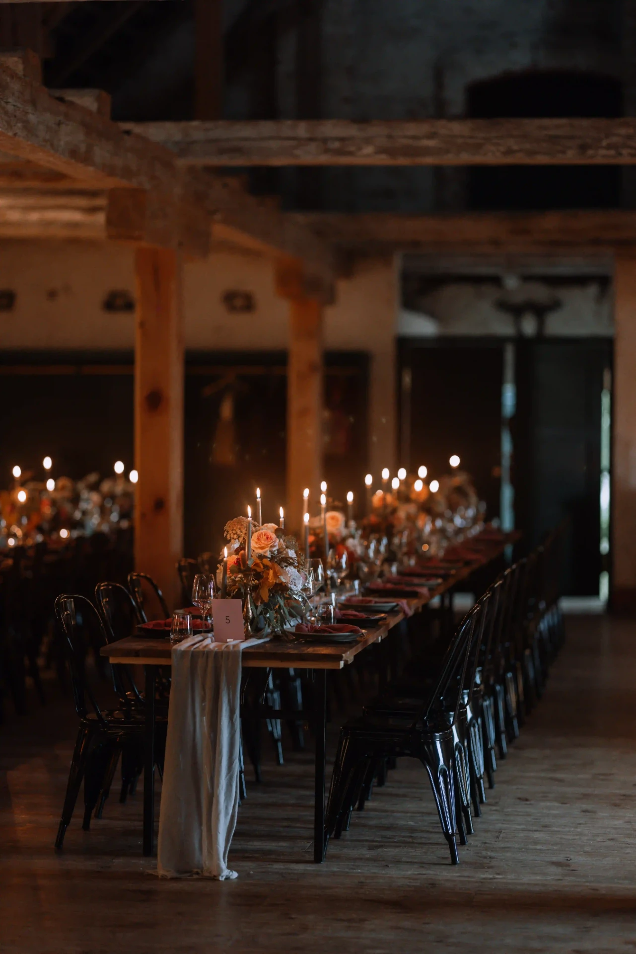 Long wedding table in a rustic barn illuminated by candlelight