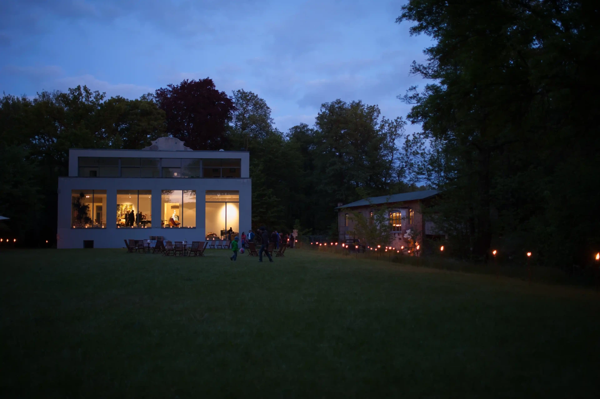 Illuminated building in the evening, surrounded by a dark garden