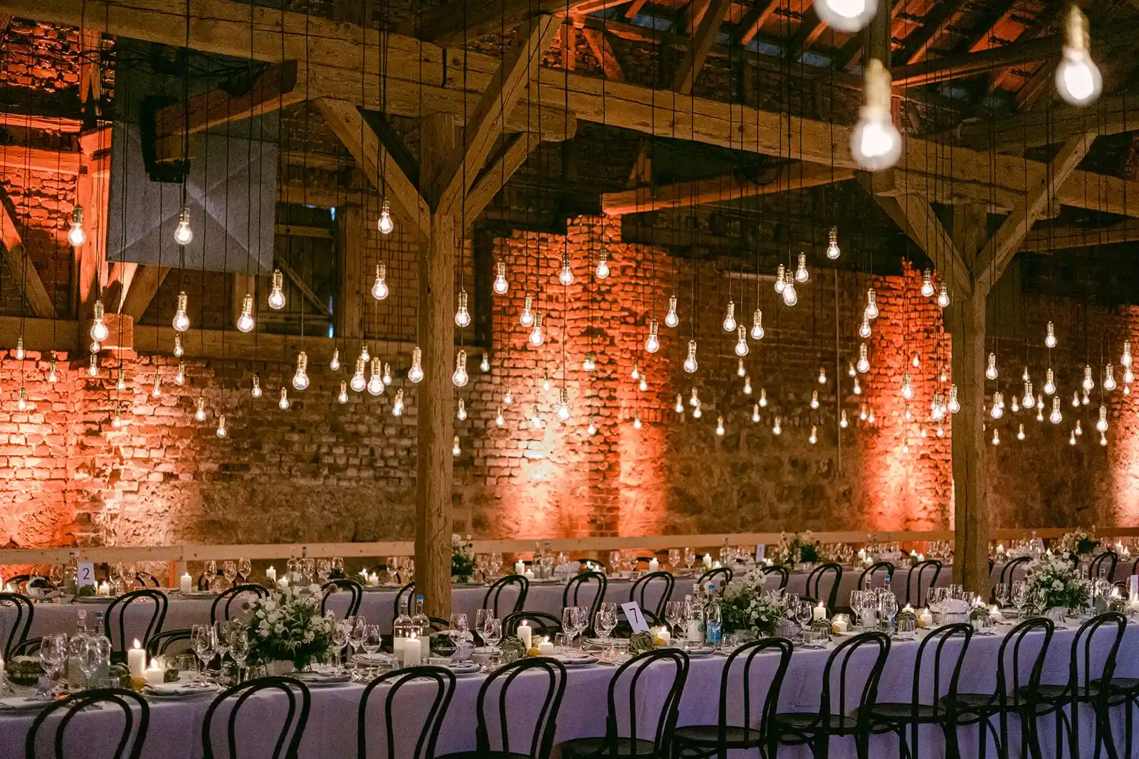 Long set tables in a barn with brick walls and warm lighting