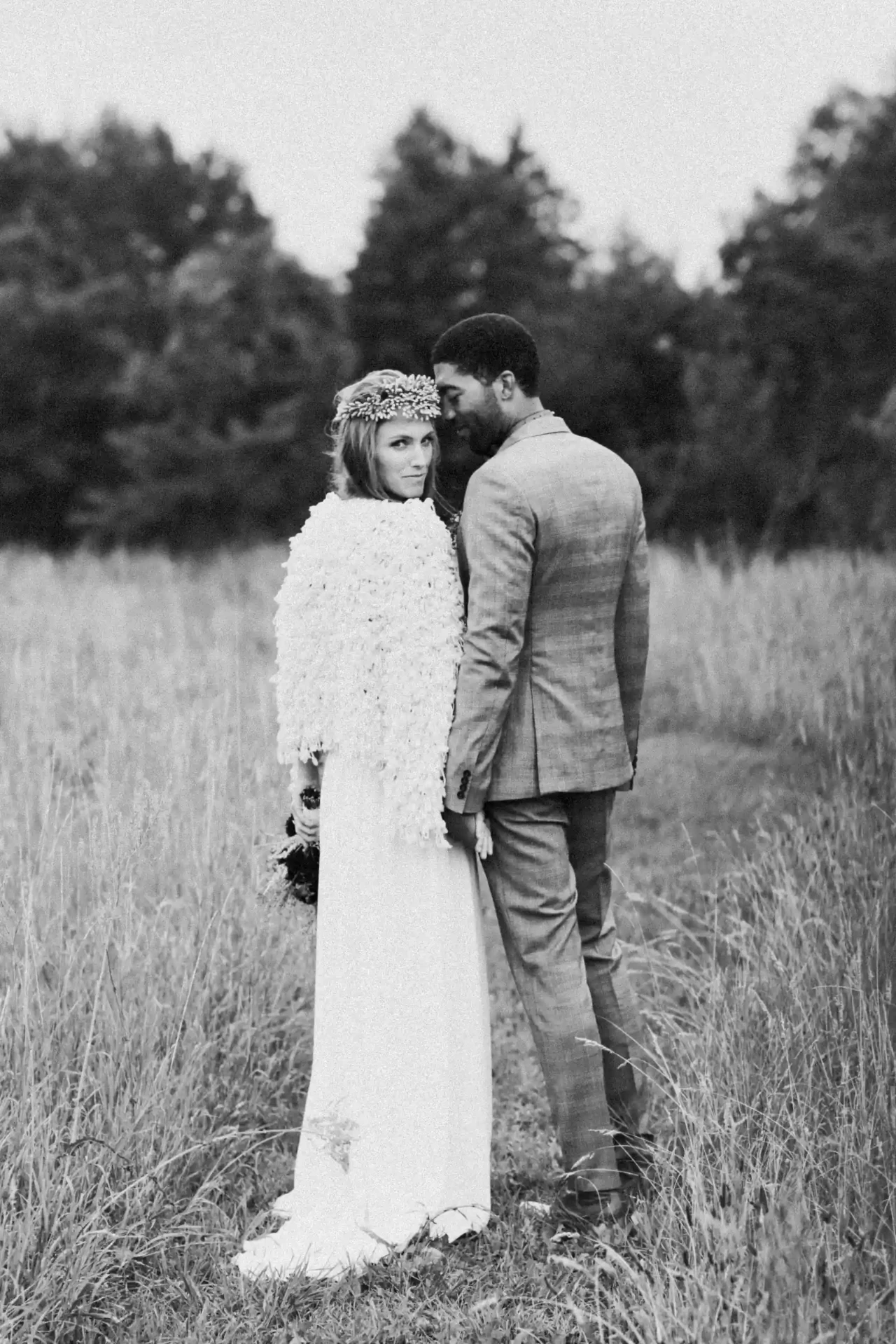 Bride and groom standing together in a meadow, black-and-white photograph