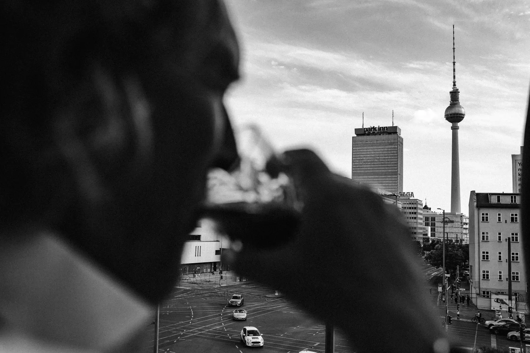 Schwarz-Weiß-Aufnahme einer Person mit Glas vor einer Stadtkulisse