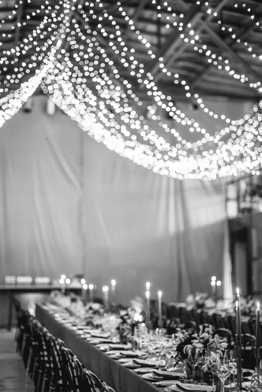 Black-and-white photograph of a long wedding table beneath many lights