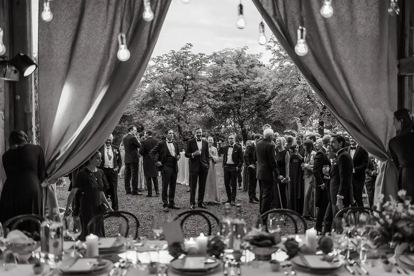 Black-and-white photograph of wedding guests beneath a draped entrance